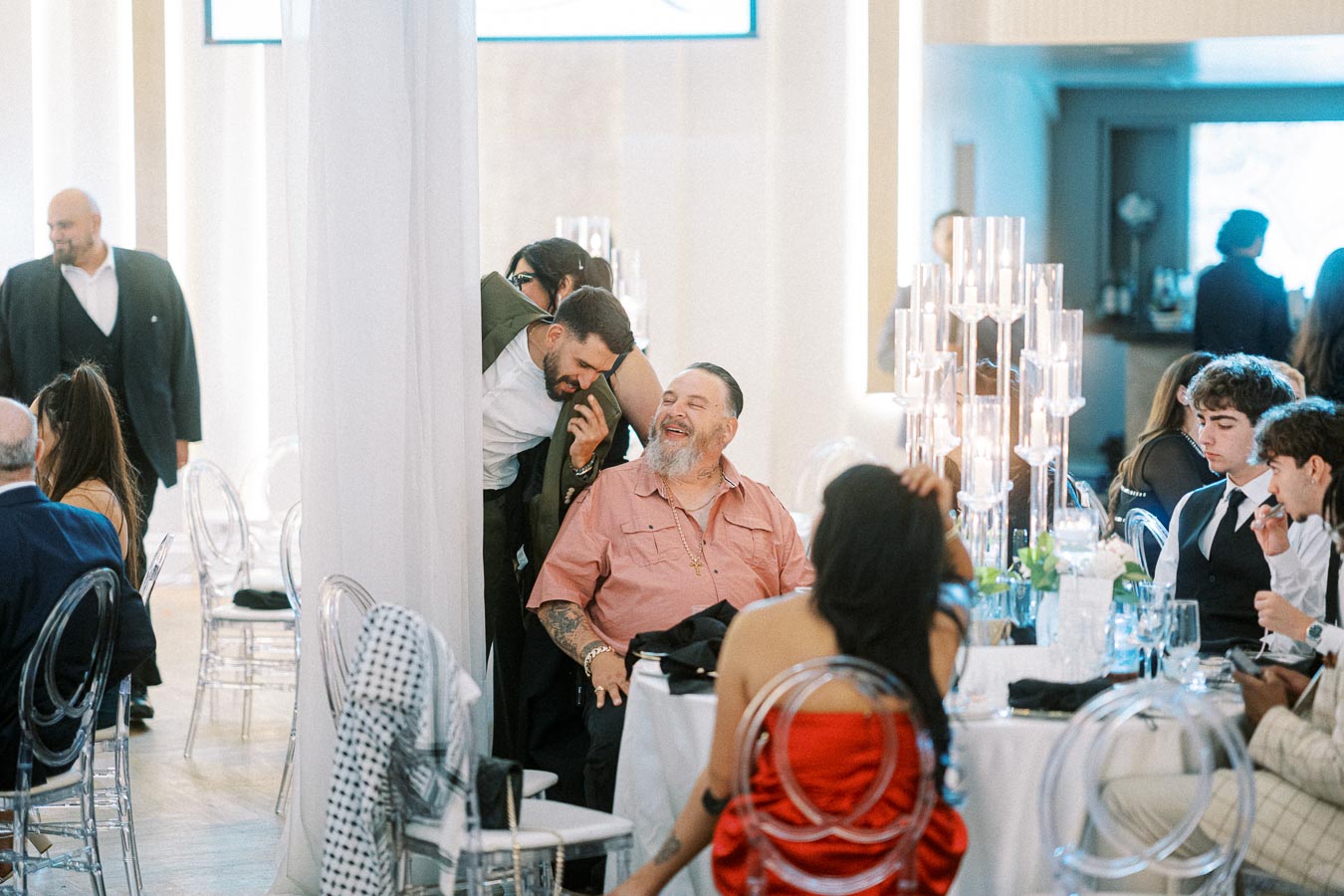 A group of people enjoying a lively conversation at an elegant indoor event, featuring modern transparent chairs and