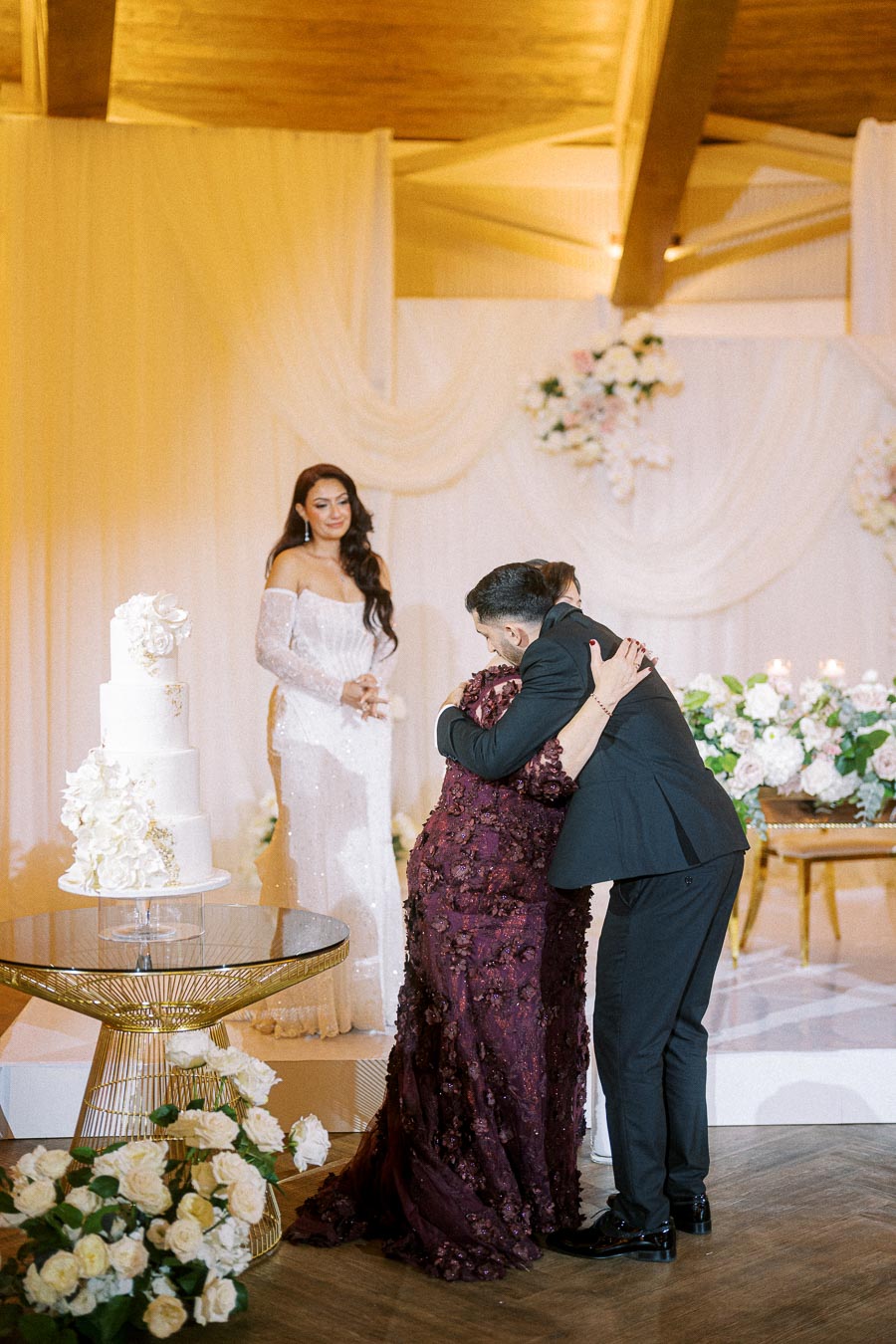 Elegant wedding scene with a couple embracing in front of a beautifully decorated table, featuring a white tiered cake