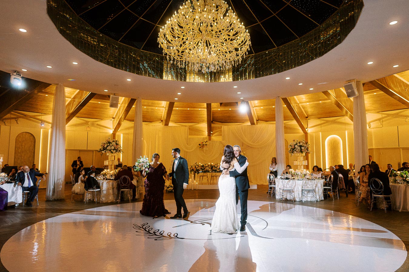 Elegant wedding reception scene with a couple dancing in the center of a lavishly decorated ballroom featuring a grand