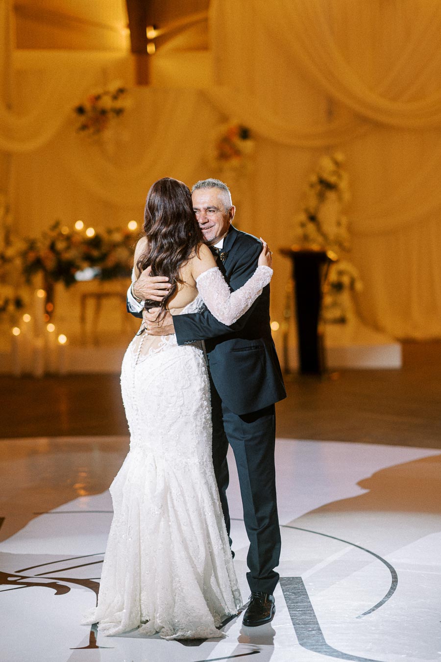 Father and bride sharing a heartfelt dance at a wedding reception, with elegant drapery and floral decorations in the