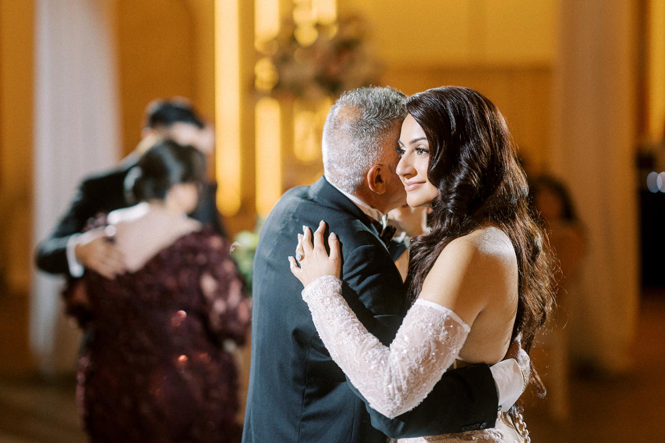 Bride and father share a heartfelt dance at a wedding reception, with other guests dancing in the background, creating a