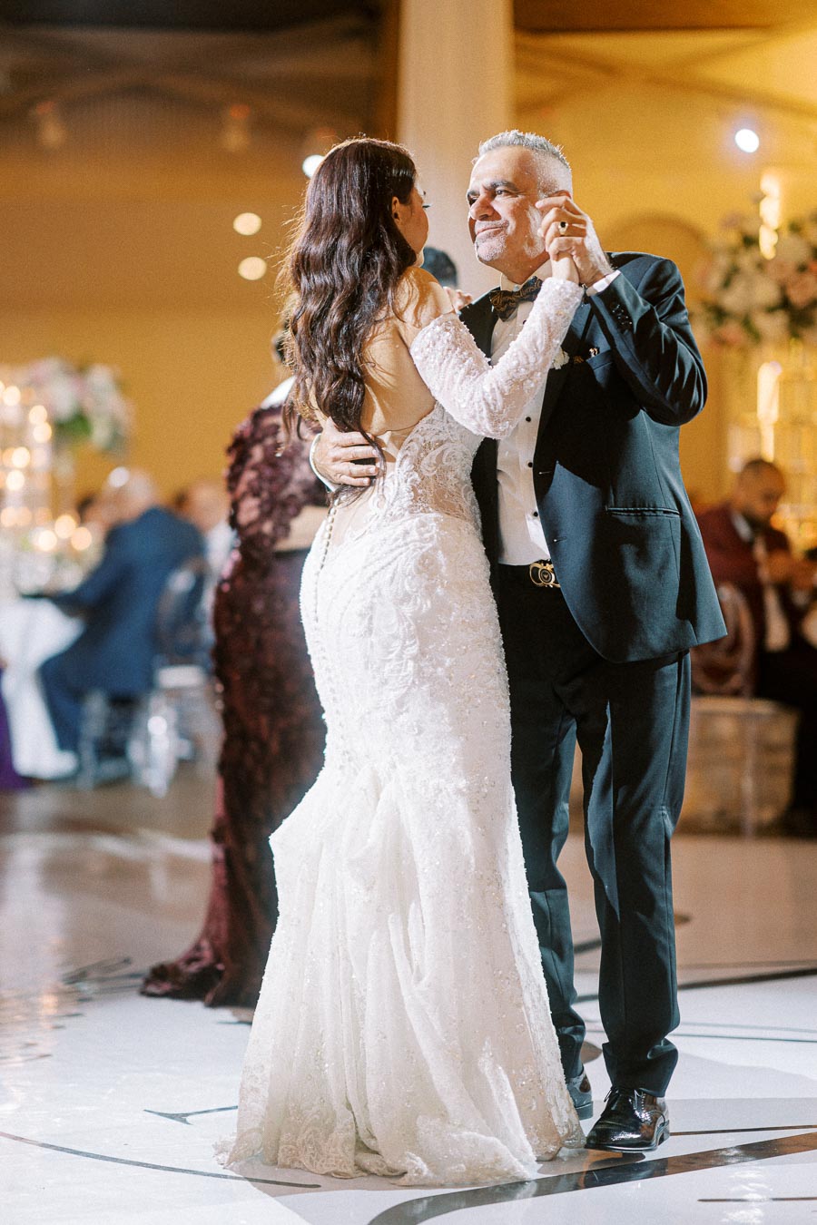 Father and bride sharing a heartfelt dance at a wedding reception, bride in an elegant white gown and father in a black
