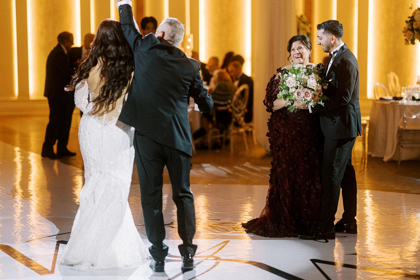 A joyful wedding reception scene with an elegantly dressed couple dancing alongside another couple, with bright, warm