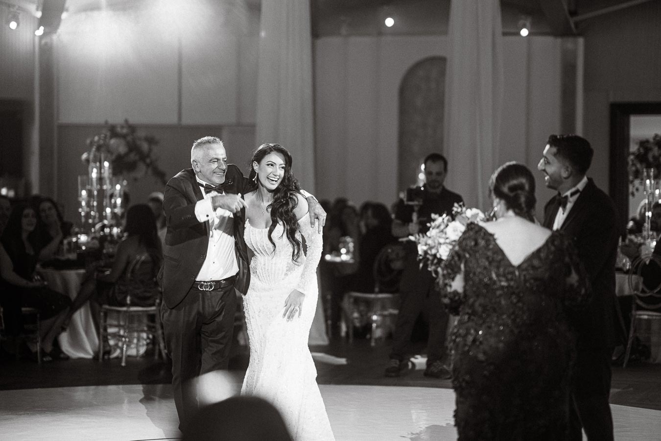 Father dancing with his daughter at a wedding reception, surrounded by elegantly dressed guests and warm lighting, capturing