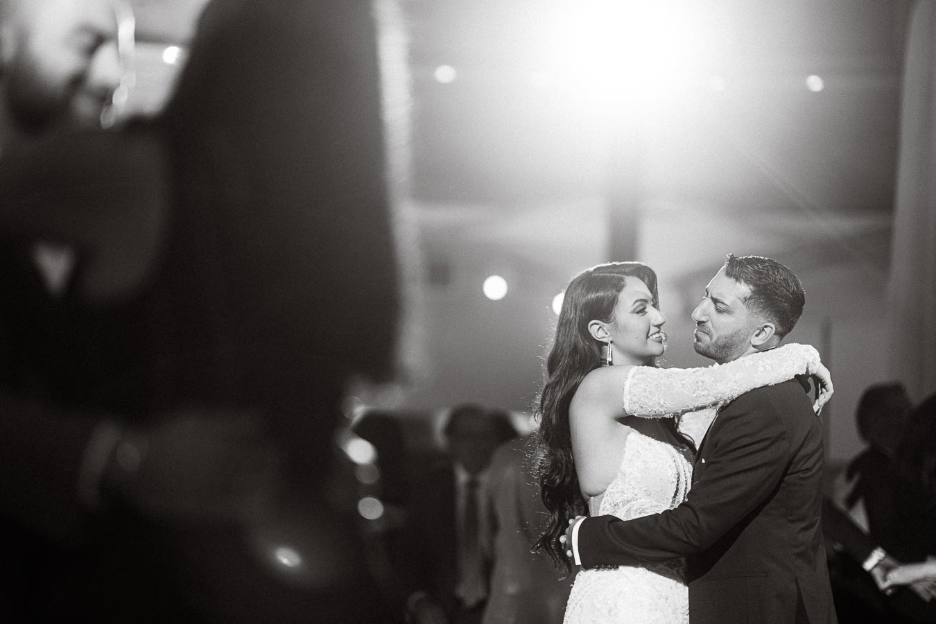 A couple sharing a romantic first dance at their wedding reception, with the bride in a lace wedding dress and the groom in
