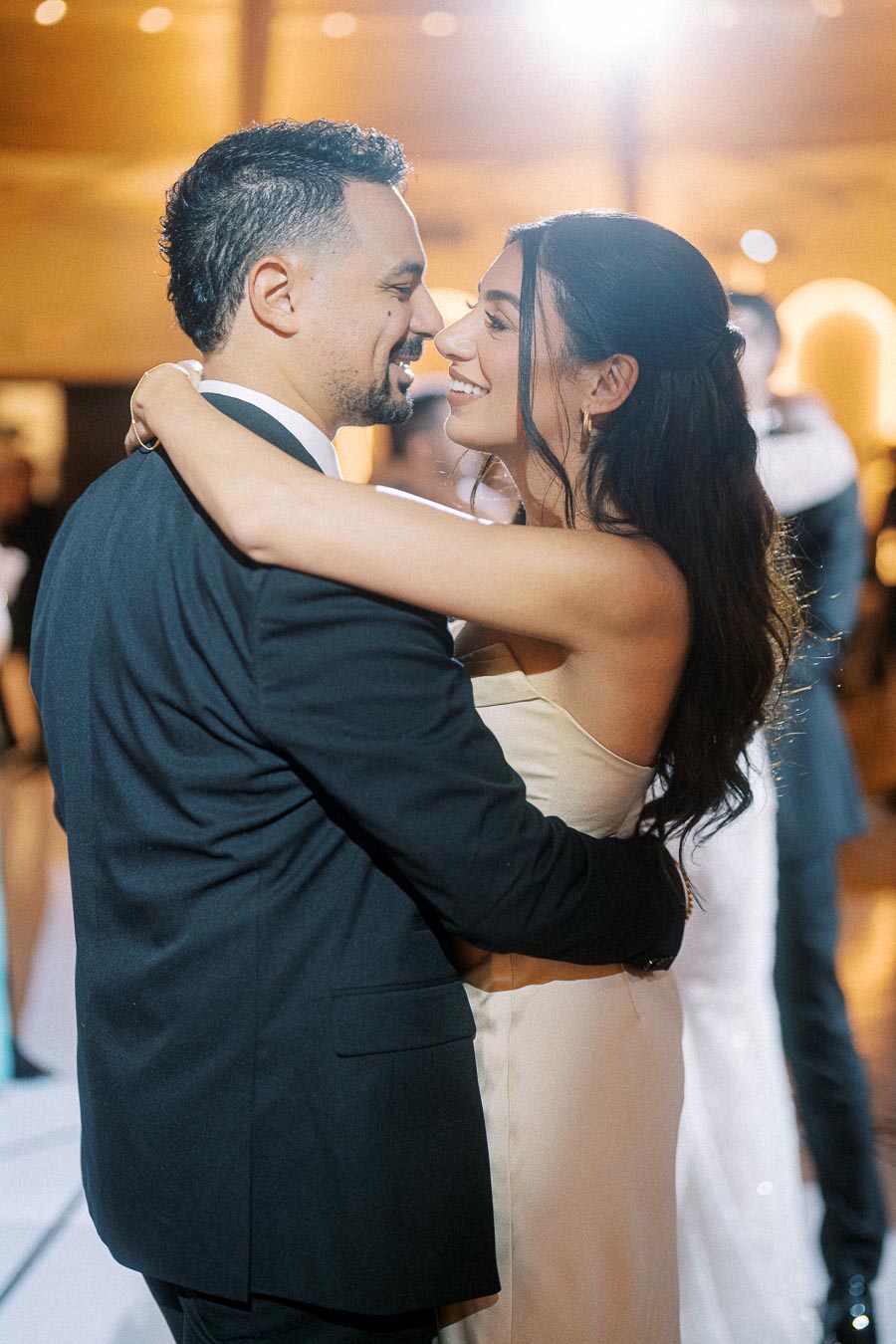 A bride and groom share a romantic first dance at their wedding reception, embracing and smiling at each other joyfully