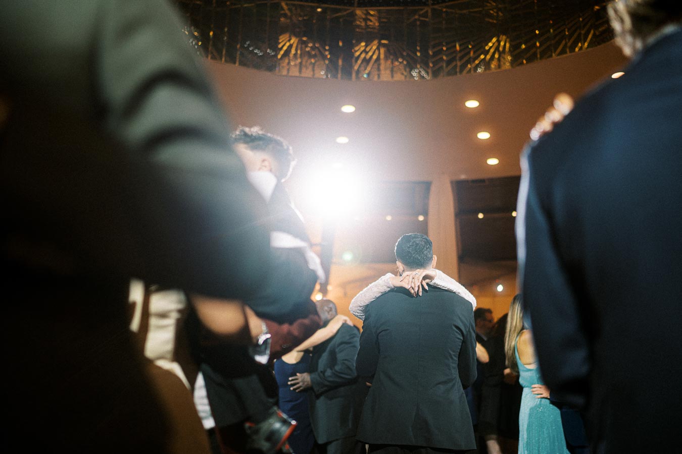 Couples dancing elegantly at a formal event, illuminated by warm, ambient lighting.