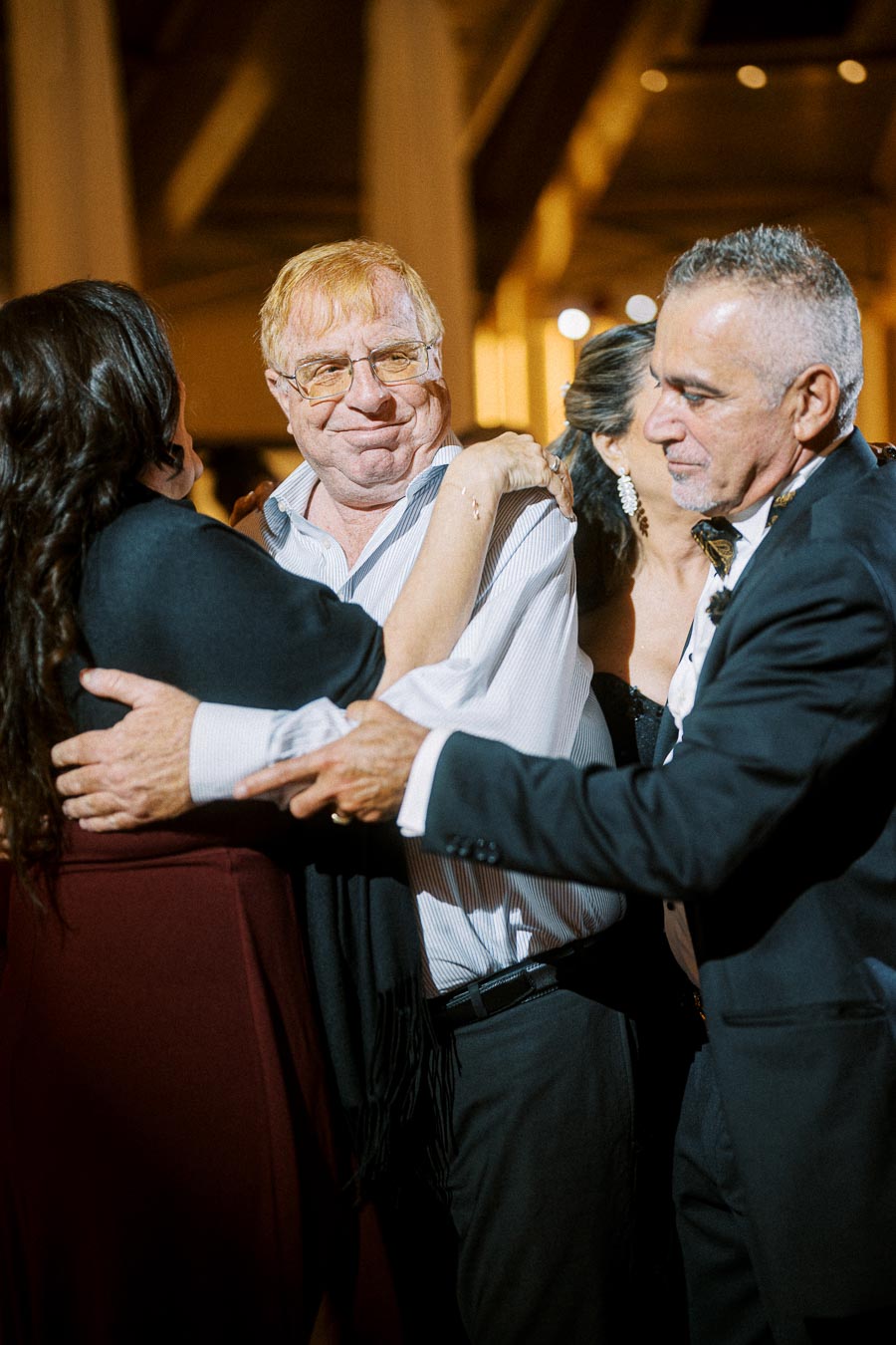 Elderly man smiling and embracing people at a joyful gathering or celebration.