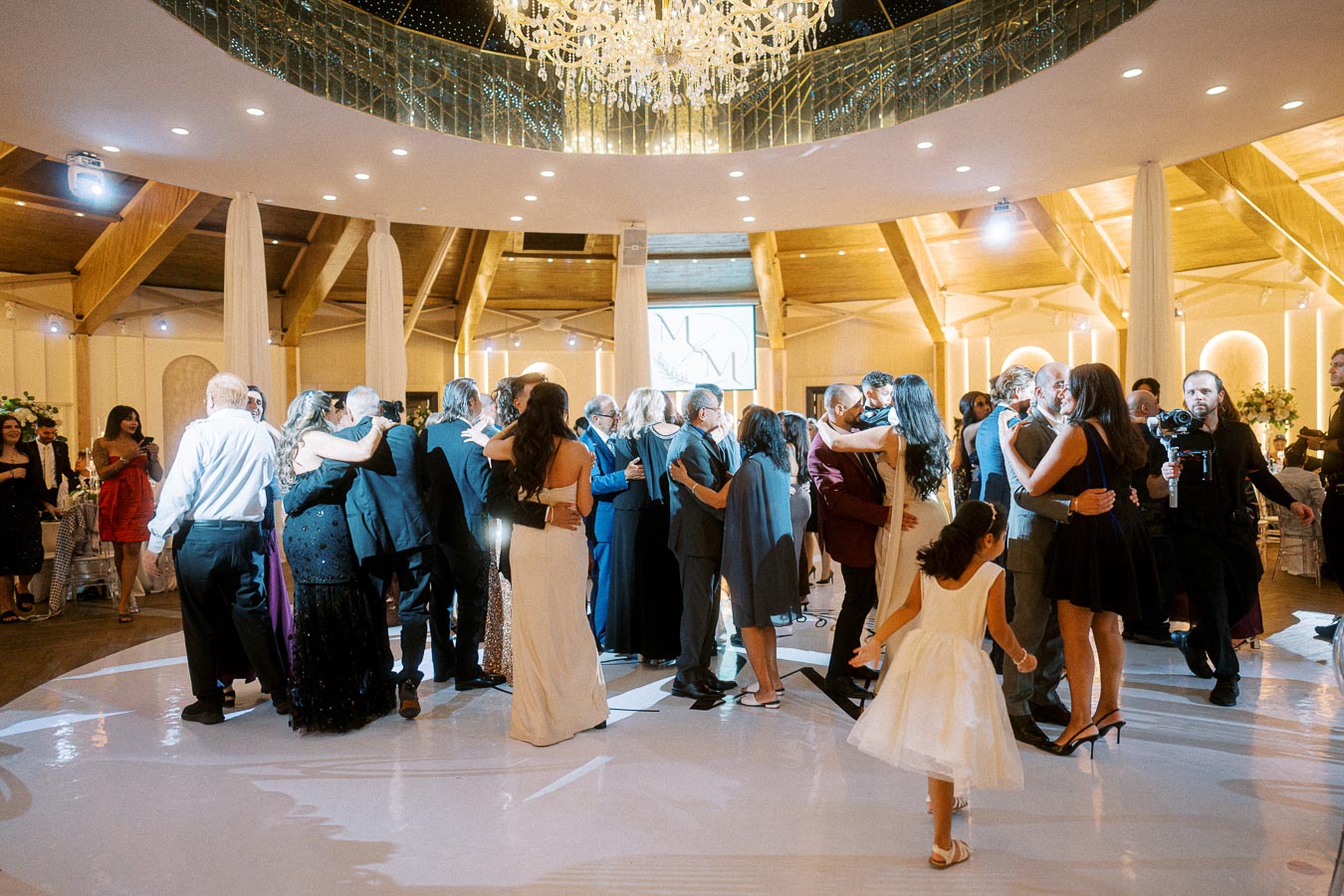 Elegant ballroom wedding reception with couples dancing under a grand chandelier, surrounded by warm lighting and a