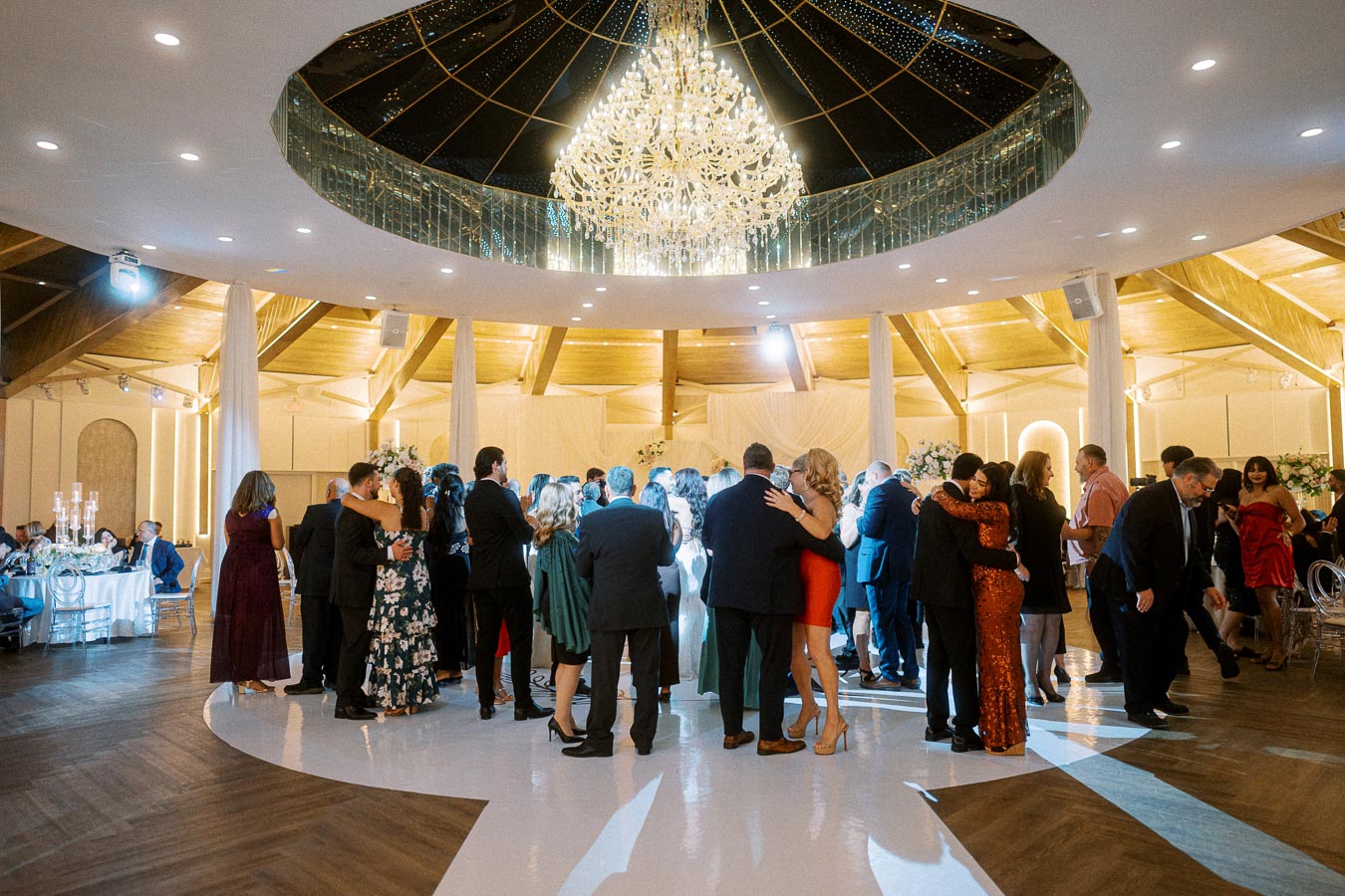Elegant ballroom wedding reception with guests dancing under a stunning chandelier, surrounded by lavish decor and ambient