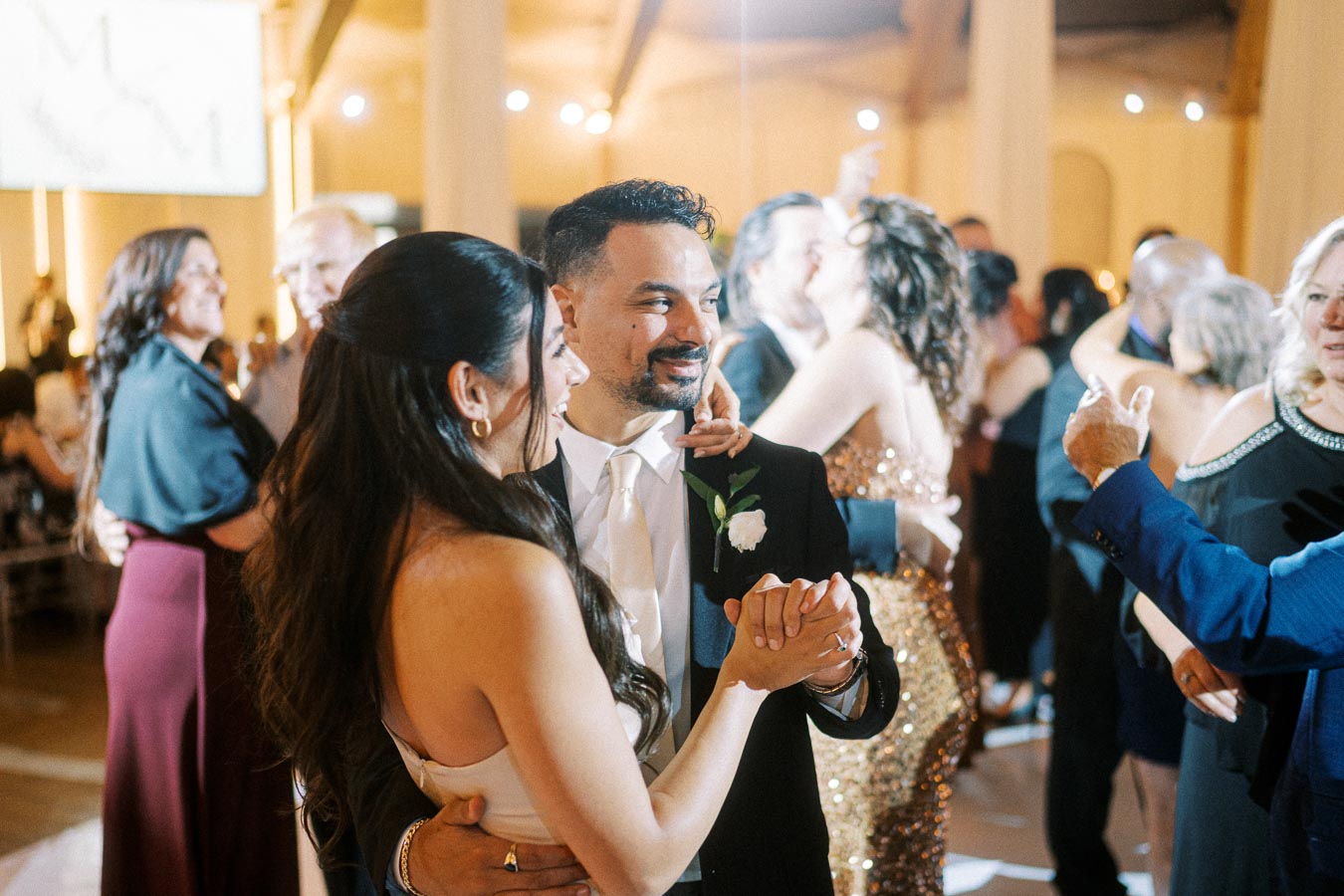 A joyous couple dances at a lively wedding reception, surrounded by guests enjoying the celebration.