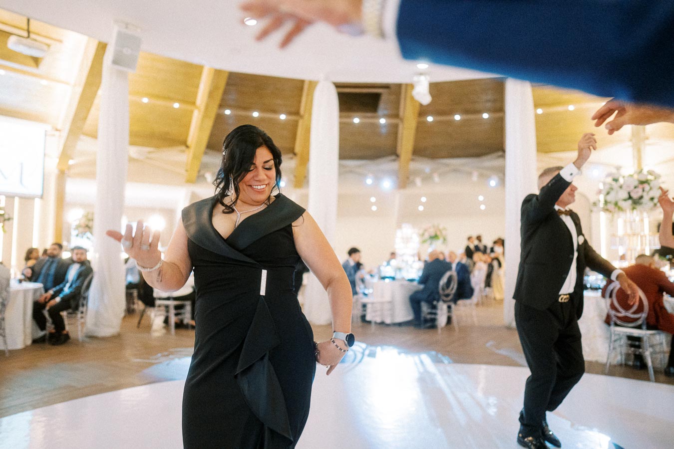 A woman in a black dress enjoying dancing at a lively event, surrounded by elegantly dressed guests.