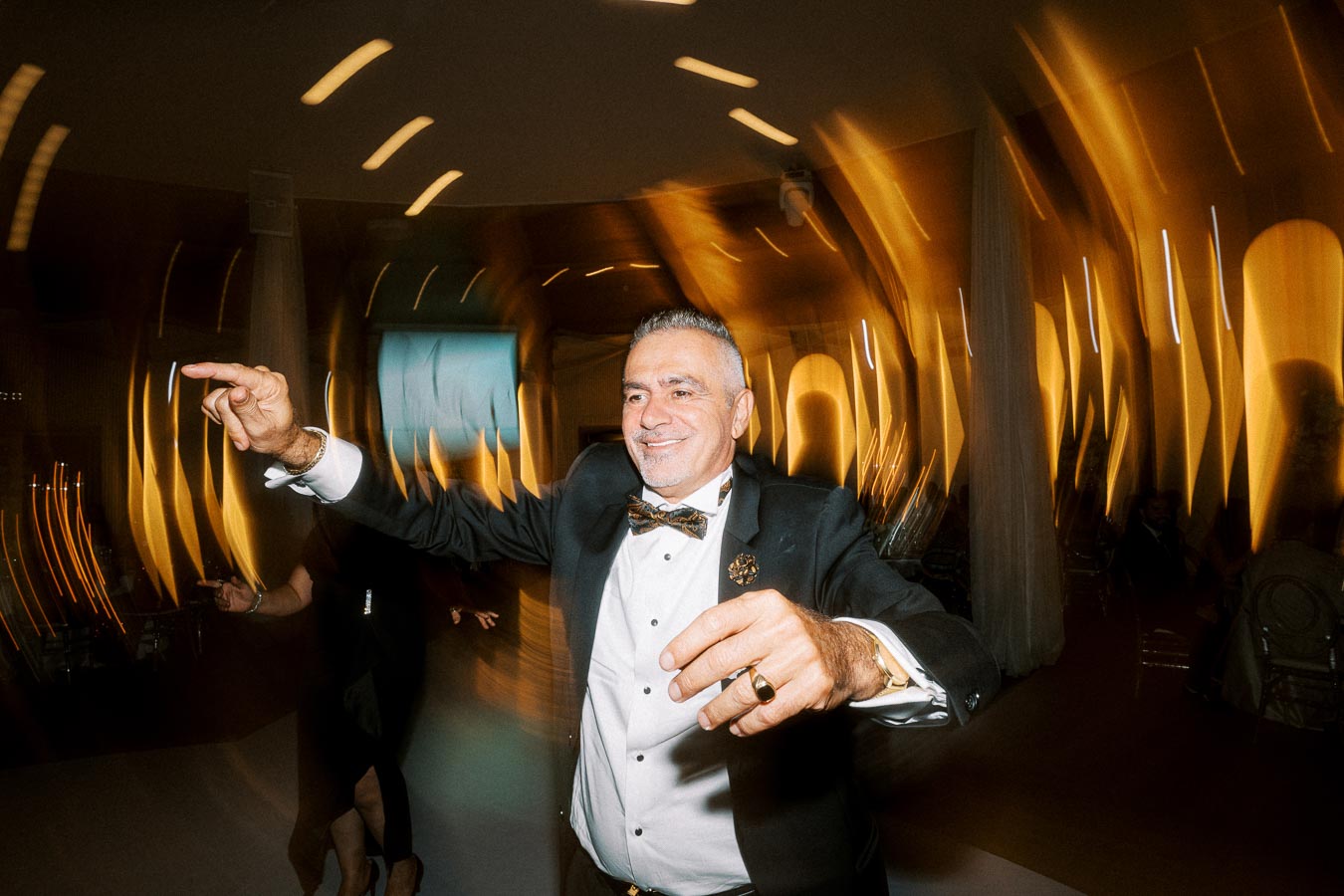 Middle-aged man in a suit joyfully dancing with dramatic light trails in a lively party atmosphere.