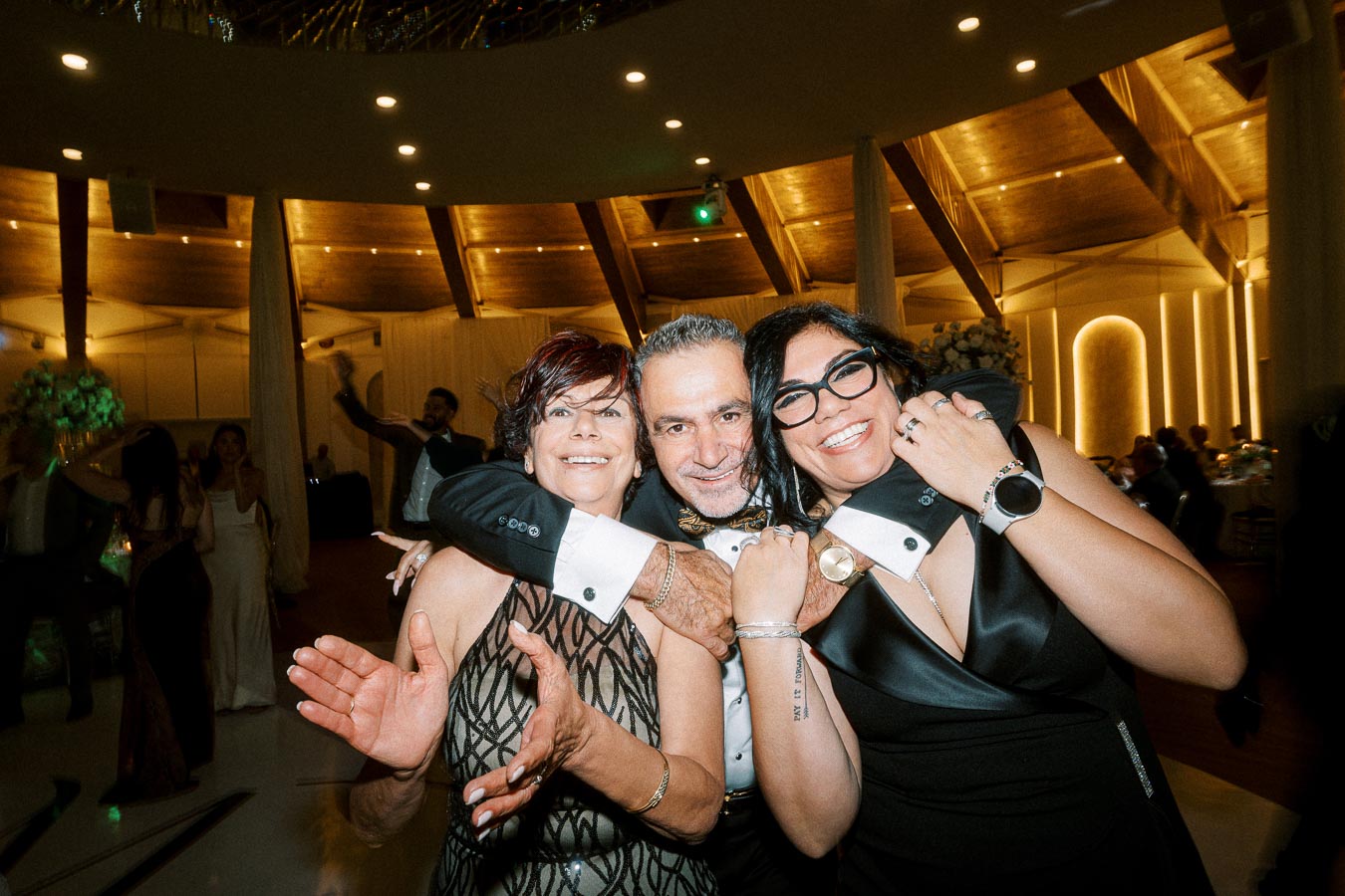 A joyful group of three people celebrating in an elegant venue, showcasing formal attire and big smiles, with a warmly lit