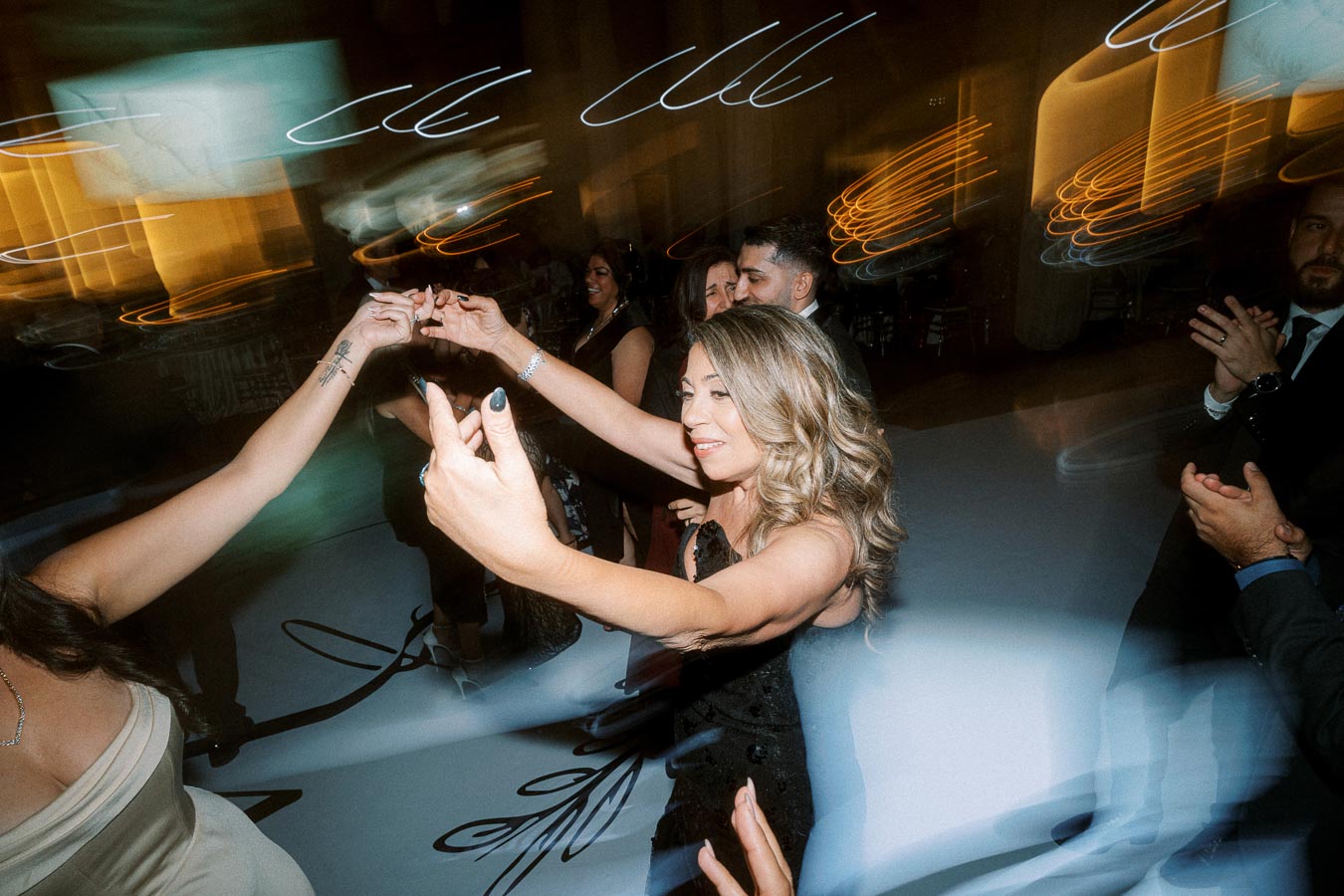 Group of people dancing energetically at a lively indoor event, with motion blur and colorful lights creating a dynamic