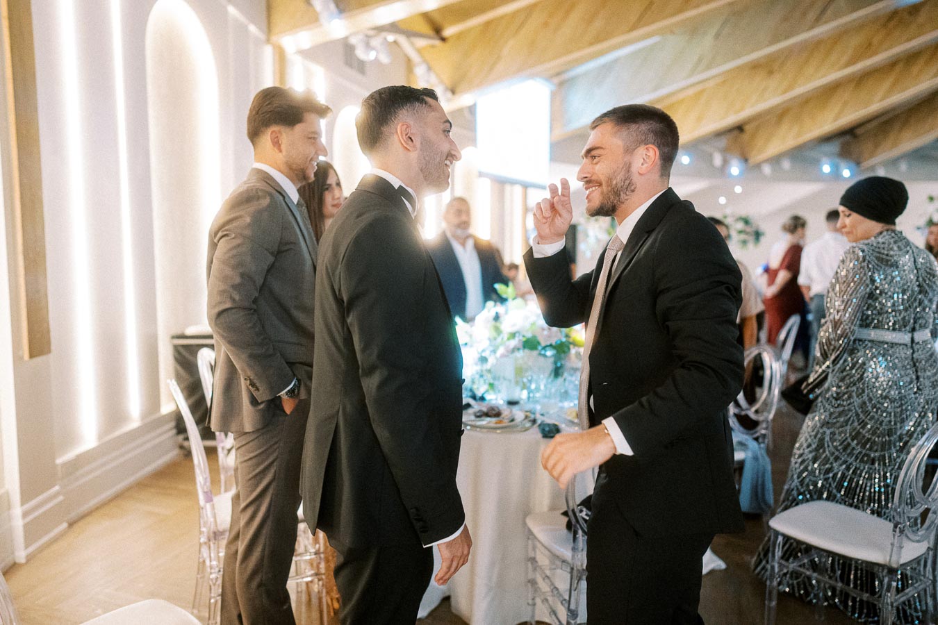 A group of well-dressed people engaging in lively conversation at a modern indoor event, featuring stylish suits and elegant