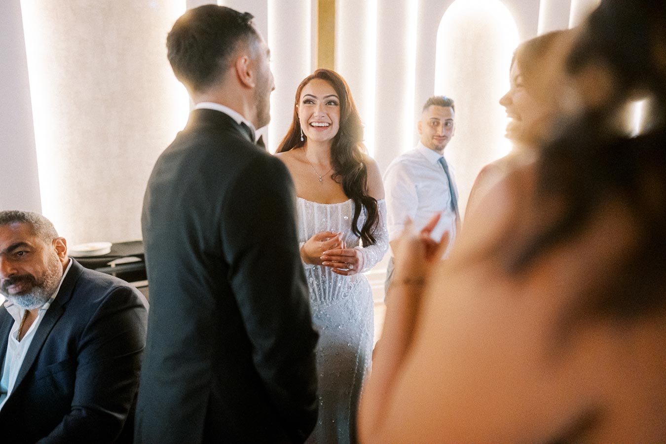 Wedding reception with elegantly dressed guests in conversation, featuring a smiling bride in a shimmering white gown and