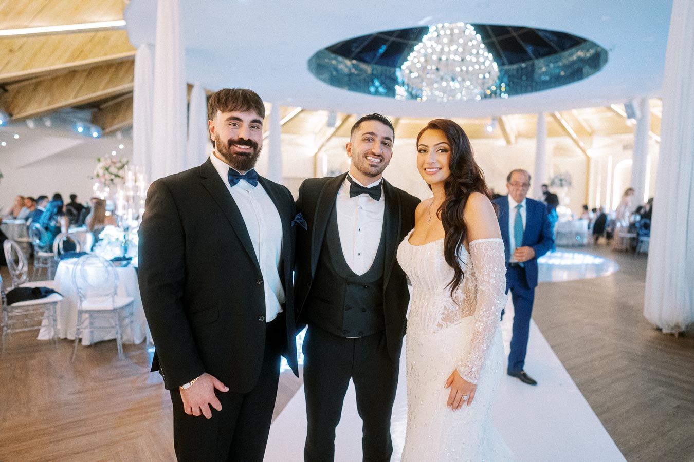 Elegant wedding reception with guests in formal attire posing indoors under a sparkling chandelier, highlighting a joyful