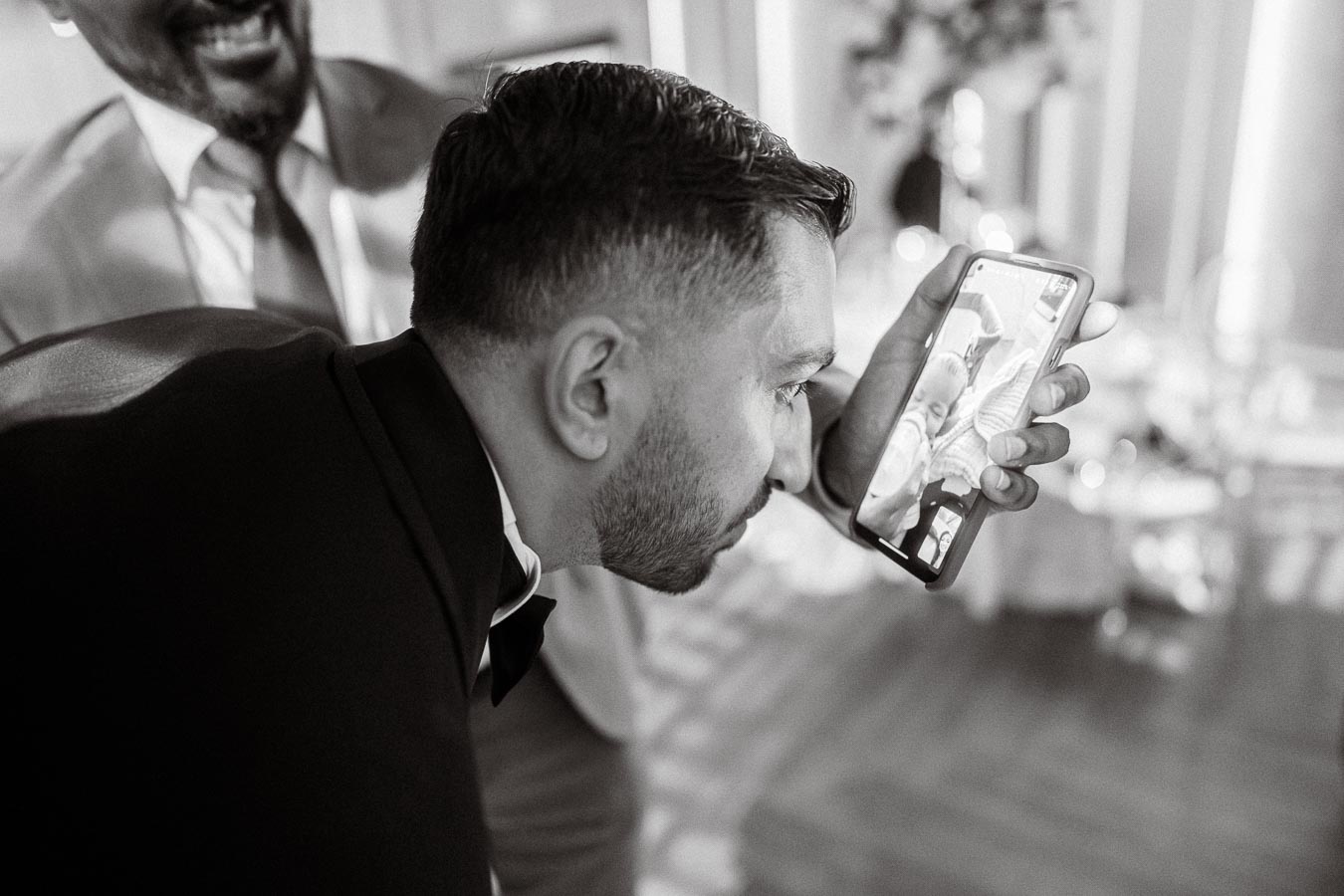A man dressed in formal attire holds a smartphone close to his face for a video call, with another person smiling in the