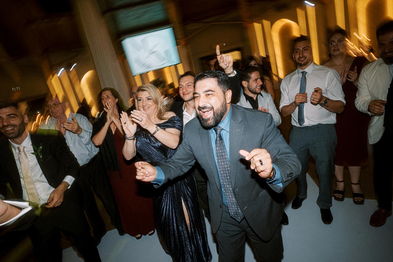A joyful group of people dressed formally, dancing and celebrating together in a well-lit indoor venue, capturing a lively