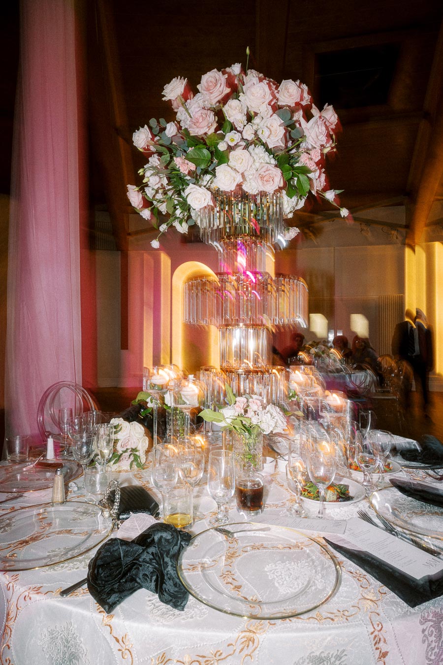 Elegant wedding reception table setting with ornate floral centerpiece featuring pink and white roses atop a crystal stand,