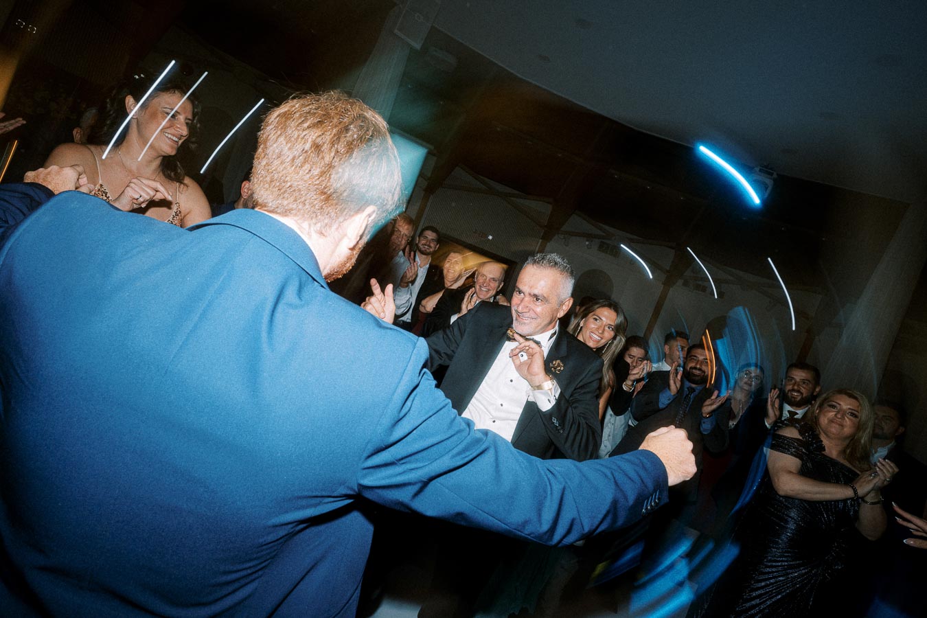 A lively group of well-dressed people dancing at an indoor event, with vibrant lighting and joyful expressions.