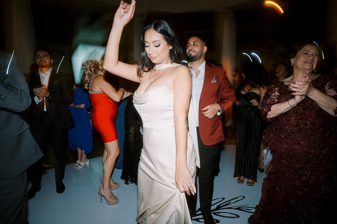 A group of elegantly dressed people dancing joyfully at a lively indoor party.