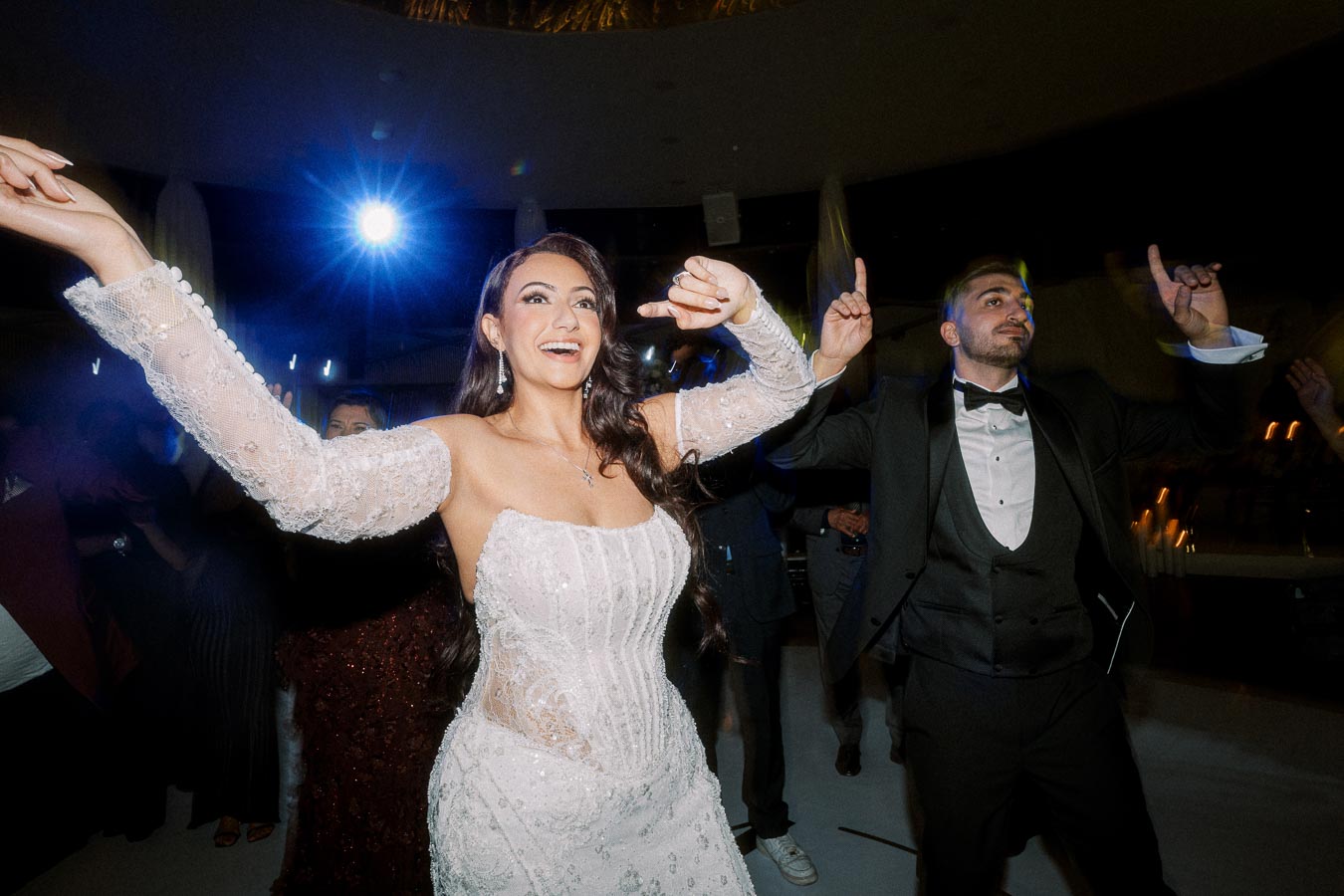 Bride and groom joyfully dancing together at their wedding reception, with the bride in a sequined lace dress and the groom