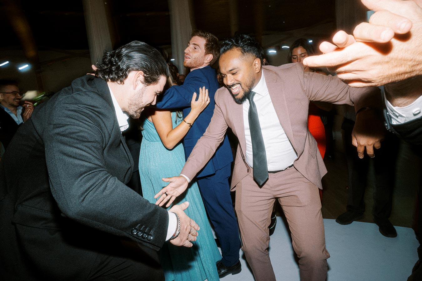 A group of people dressed in formal attire enthusiastically dancing at a lively party, highlighting joyful interactions and