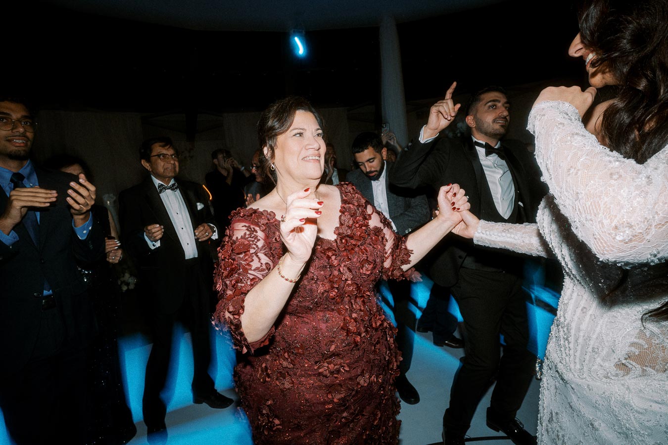 Dancing guests enjoy a joyful celebration at a formal event, dressed in elegant attire, with a woman in a red lace dress