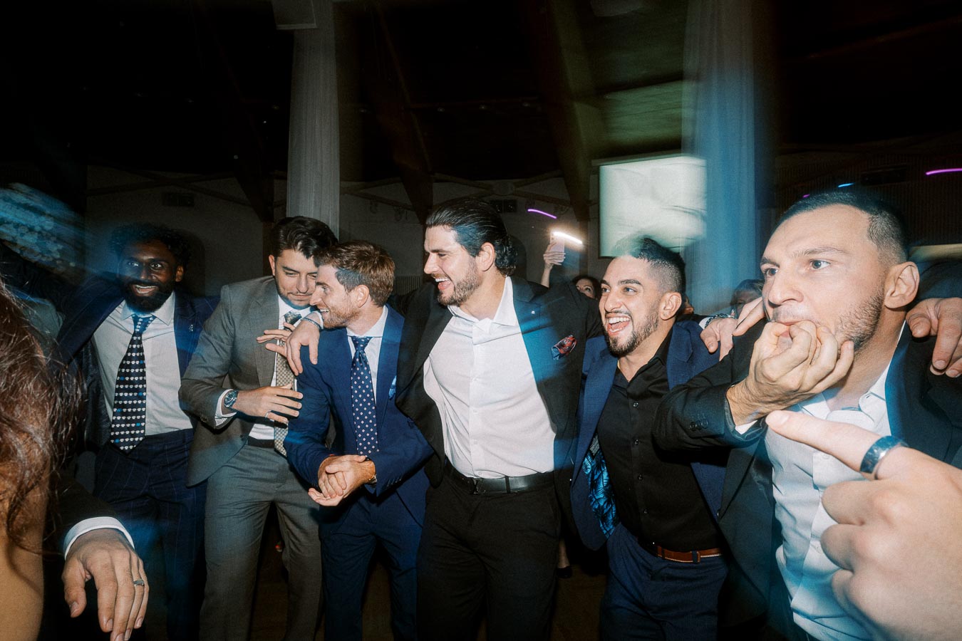 A group of men in formal attire joyfully celebrate and embrace each other at a lively event, showcasing camaraderie and