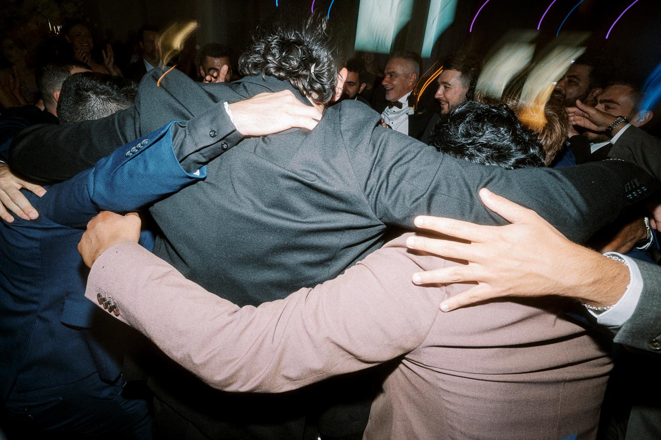 A joyous group celebration featuring people in formal attire with their arms around each other, enjoying a lively event with