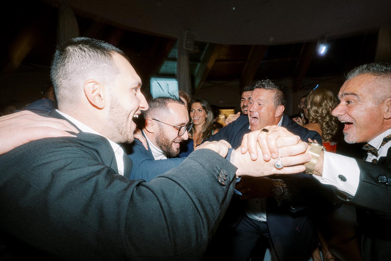 Group of well-dressed people joyfully celebrating at an event, embracing and laughing together indoors.