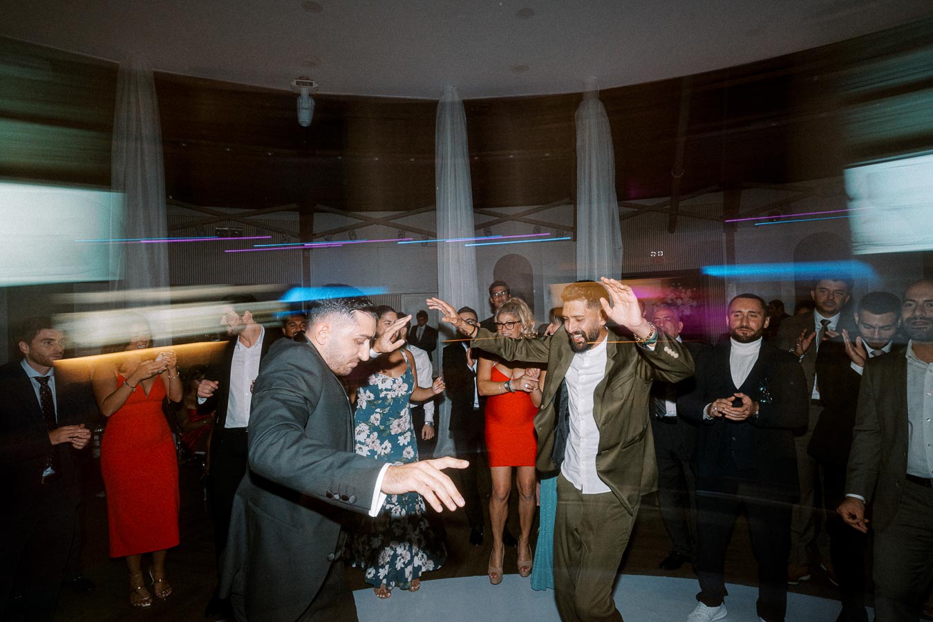 A lively wedding reception with guests dancing energetically on the dance floor, featuring blurred motion trails from