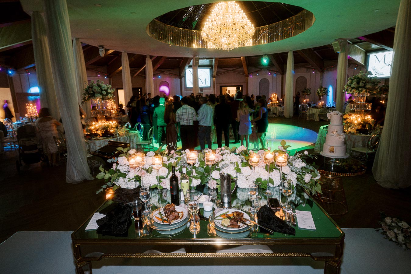 Luxurious wedding reception venue with elegant table setting, featuring floral centerpieces, candlelit ambiance, and a grand