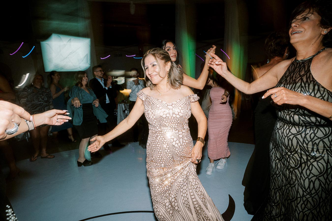 A joyful group of people dancing at an evening event, featuring a woman in an elegant patterned gown smiling as she enjoys