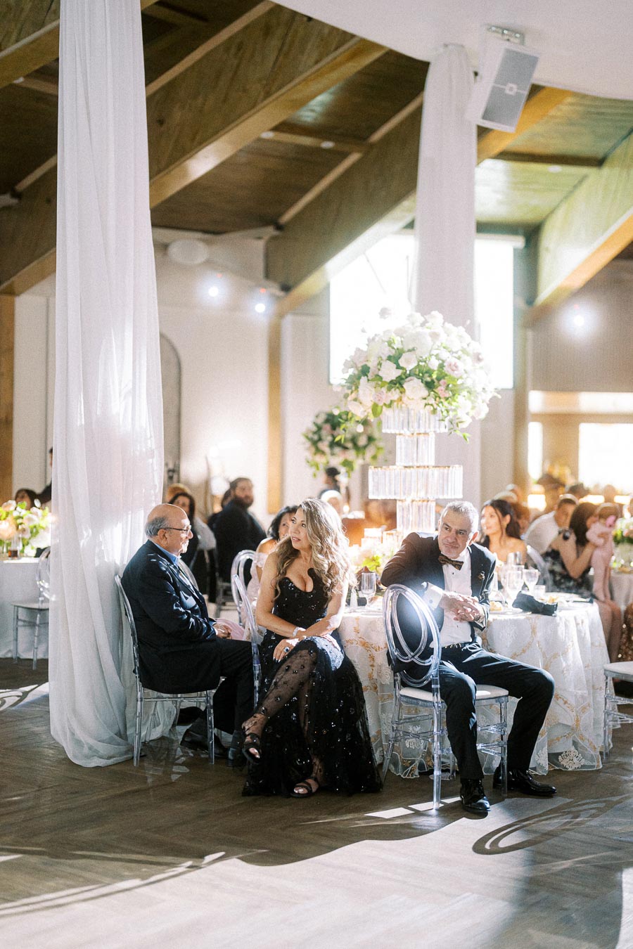Elegant wedding reception with guests seated at a beautifully decorated round table with a tall floral