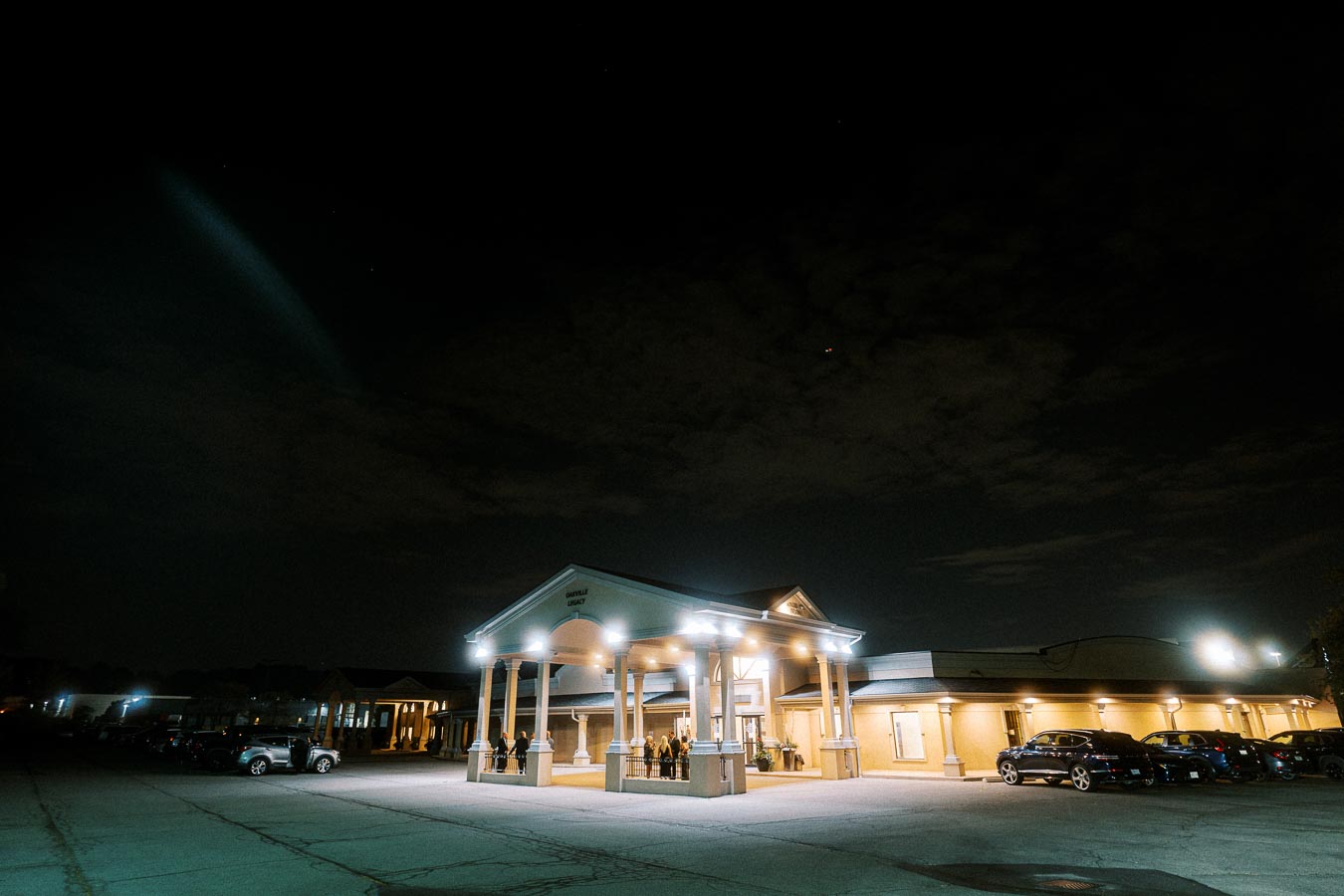 Exterior view of a well-lit building at night, with cars parked in the lot and a clear night sky above.