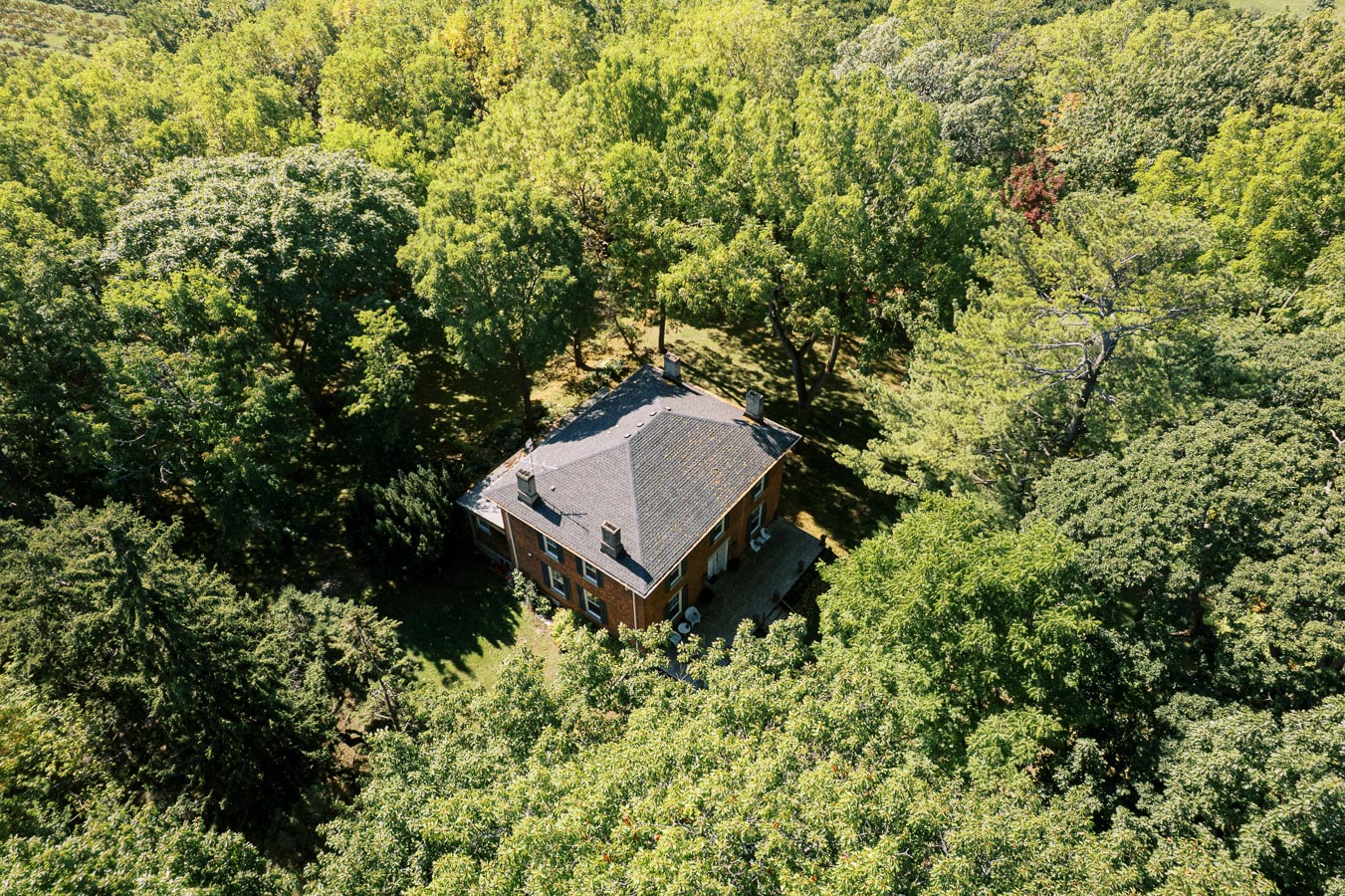 Aerial view of a secluded brick house surrounded by dense green forest, showcasing a peaceful and private natural setting ideal for nature lovers and those seeking tranquility.