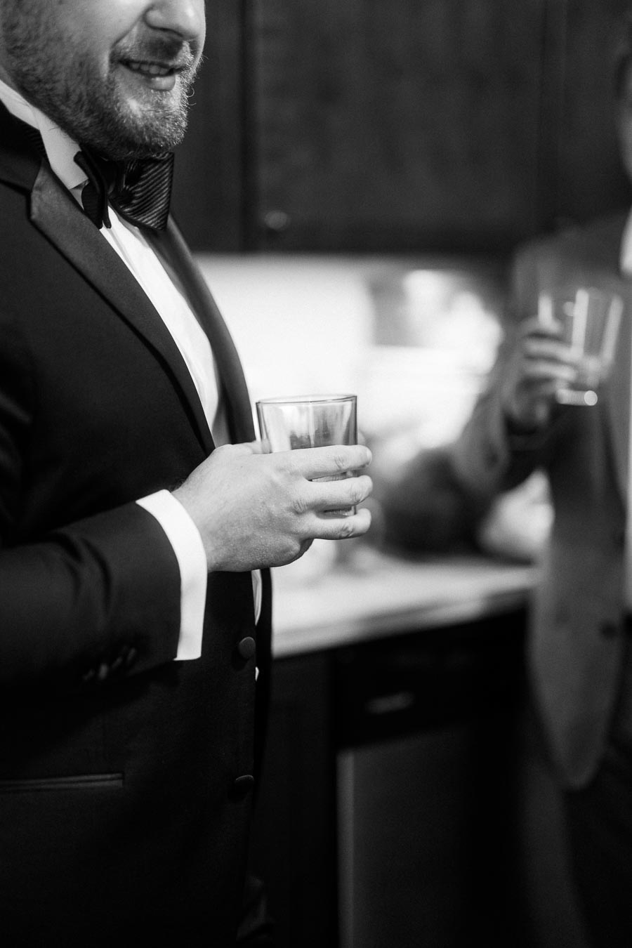 Black and white image of a man in a suit holding a glass, with another person in the background, possibly at a formal event or celebration.