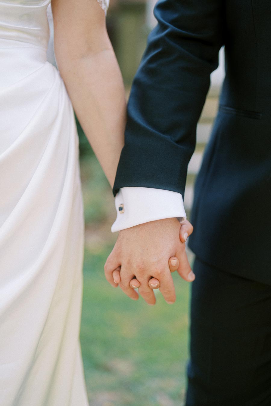 Couple holding hands in wedding attire, featuring a bride in a white dress and a groom in a dark suit, symbolizing love and commitment.