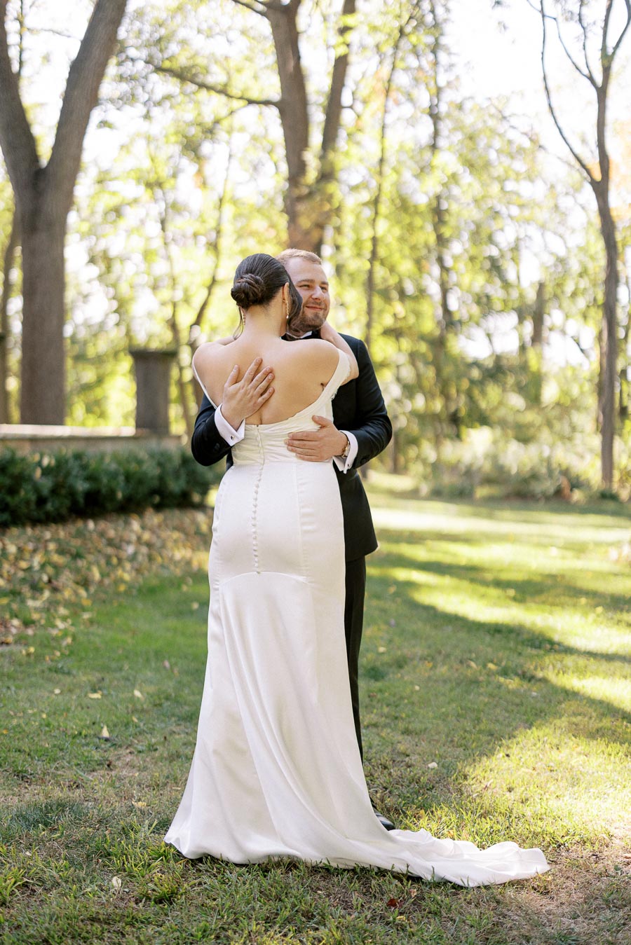 Bride and groom embracing outdoors in a lush green garden, sunlight filtering through the trees, capturing the joy and romance of their wedding day.