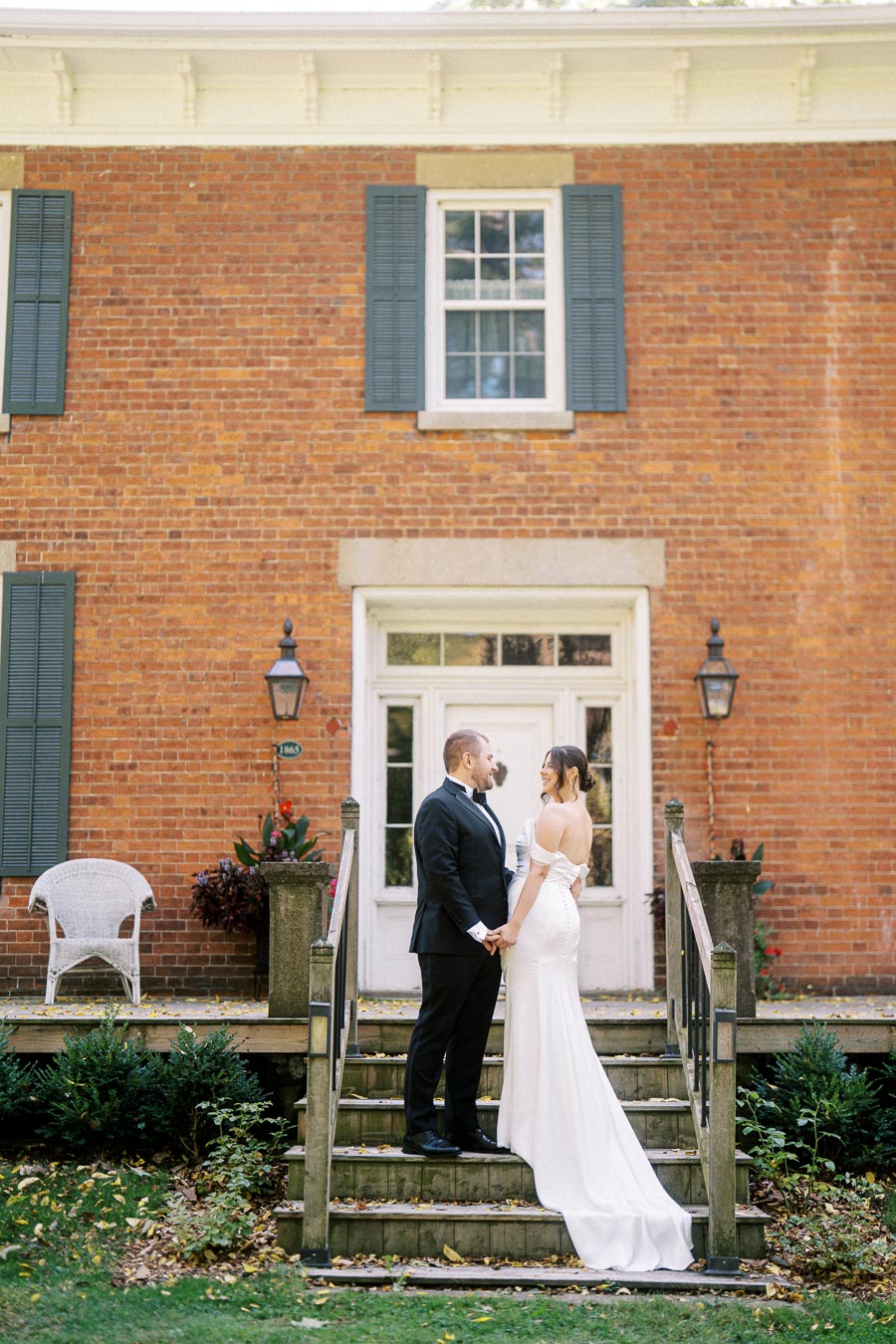 Wedding couple holding hands on stairs of vintage brick building with blue shutters and white trim.