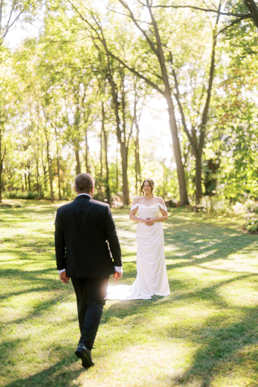Bride and groom in an outdoor garden setting, surrounded by sunlight and lush green trees, capturing a romantic moment in a wedding ceremony.