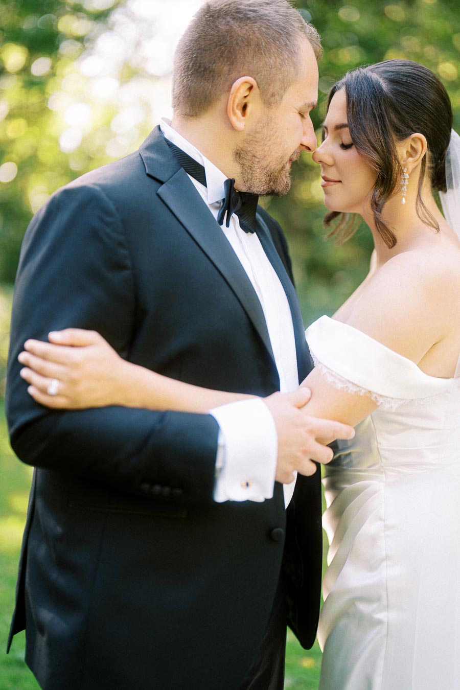 A bride and groom embracing intimately in a lush green outdoor setting, both elegantly dressed in a tuxedo and wedding gown, conveying love and romance on their wedding day.