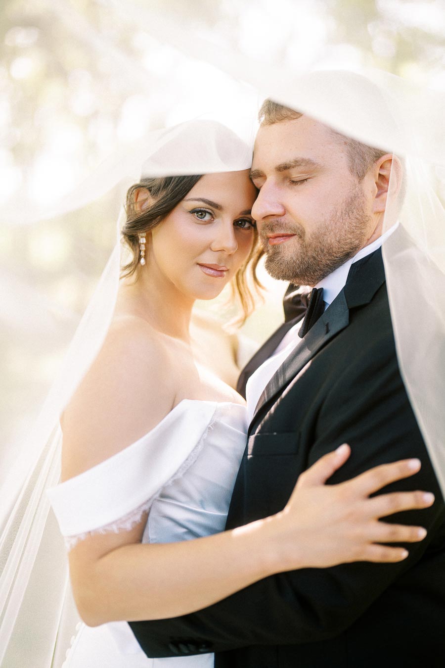 Elegant bride and groom embracing under a veil, capturing a tender wedding moment with soft natural lighting.