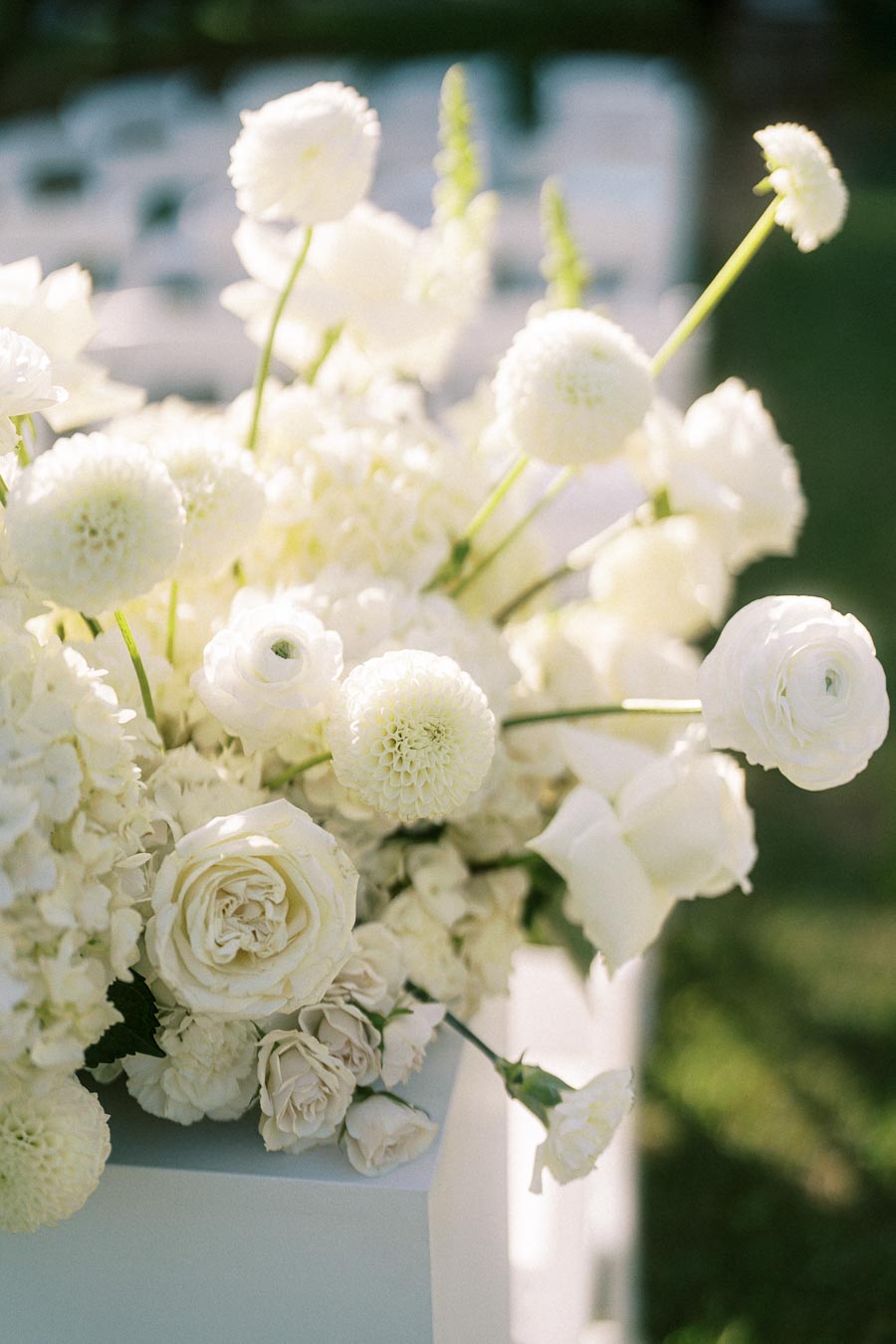 Elegant white floral arrangement with roses and dahlias in outdoor setting, ideal for weddings or special events.