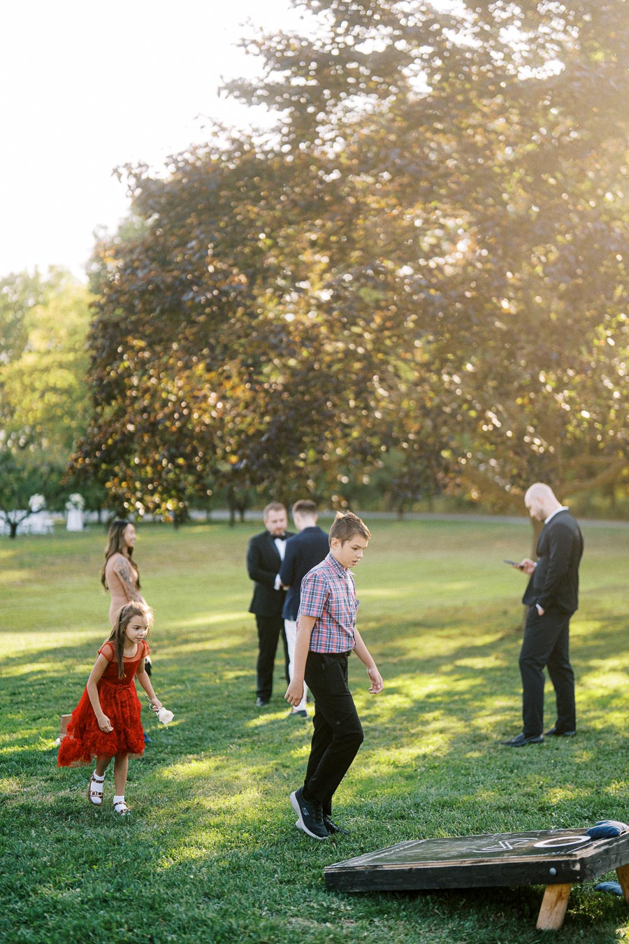 Outdoor gathering on a sunny day with adults and children playing a lawn game in a park setting.