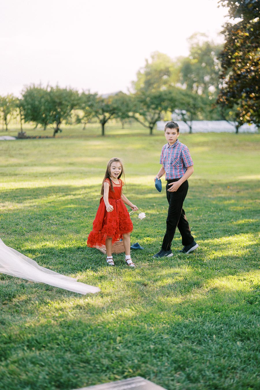 A young girl in a red dress and a boy in a plaid shirt playing on a sunny day in a green park.
