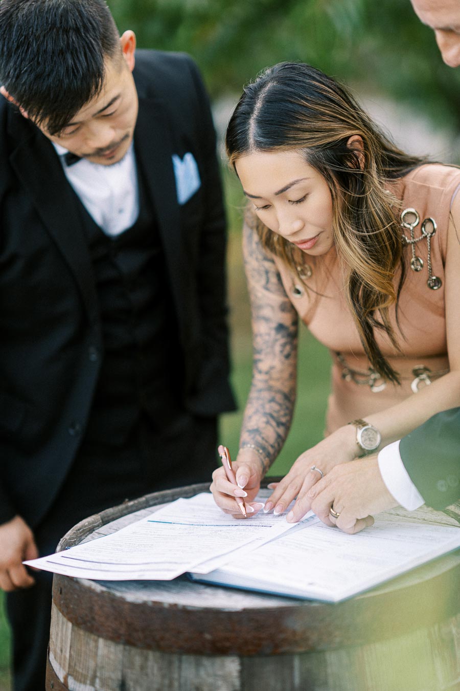 People signing a document on a wooden barrel top, focusing intensely.